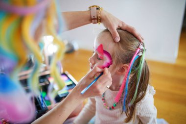Children face painting. Artist painting little preschooler girl like unicorn on a birthday party. Creative activities for kids clipart