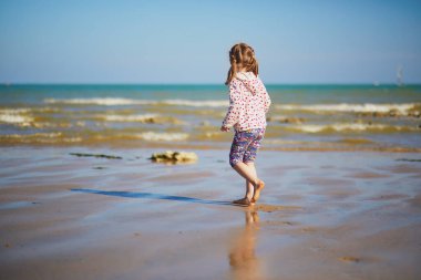 Preschooler girl having fun on the sand beach at Atlantic coast of Normandy, France. Outdoor summer activities for kids