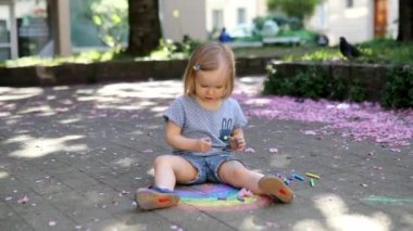 Parktaki asfalta renkli tebeşirlerle gökkuşağı çizen sevimli küçük kız çiçek açan kiraz ağaçlarıyla birlikte. Küçük çocuklar için açık hava aktiviteleri ve yaratıcı oyunlar