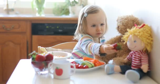 可爱的蹒跚学步的小女孩午餐吃新鲜水果和蔬菜 在厨房里喂小孩娃娃和玩具熊 儿童的美味健康食品 — 图库视频影像