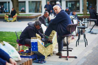 İSTANBUL, TURKEY - 20 Nisan 2023: Ayakkabı parlatıcı çoklu ağda ve sünger kullanarak ayakkabı boyama. Müşterisi taburede oturuyor, ayağı yukarıda..