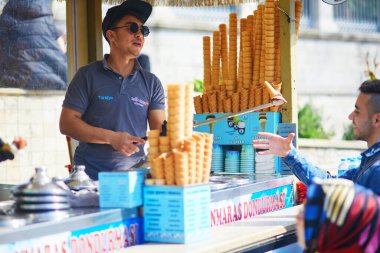 ISTANBUL, TURKEY - 25 Nisan 2023: Satıcı dondurma külahını çubuğa koyar ve müşteriye vermeden önce onu döndürerek, havaya atarak almaya çalışınca alır