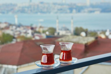 İstanbul, Türkiye 'nin Asya yakasındaki Uskudar ilçesinin çatıları manzaralı sıcak siyah çay dolu bir lale şeklinde iki Türk bardağı