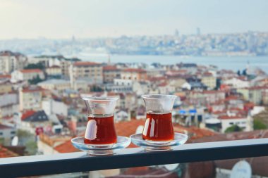 İstanbul, Türkiye 'nin Asya yakasındaki Uskudar ilçesinin çatıları manzaralı sıcak siyah çay dolu bir lale şeklinde iki Türk bardağı