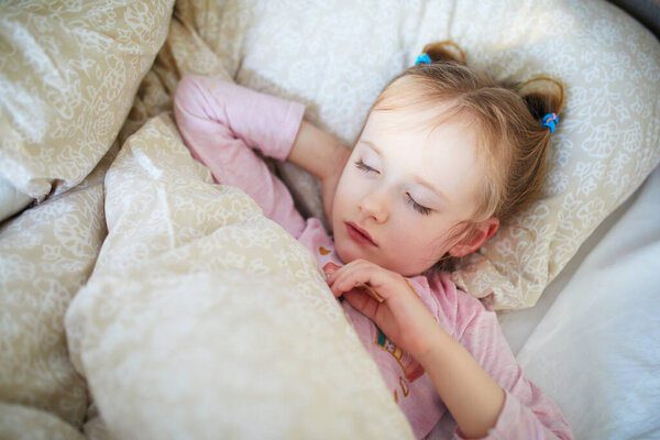 Adorable preschooler girl having a day nap. Little child sleeping in bed. Bedtime concept