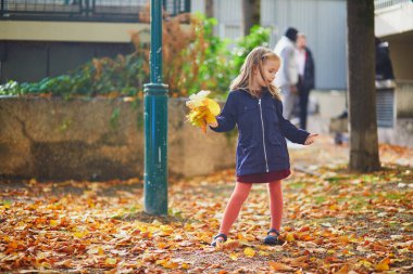 Sevimli anaokulu kızı dışarıda güneşli ve güzel bir sonbahar gününün tadını çıkarıyor. Mutlu çocuk Paris, Fransa 'da sonbahar yaprakları topluyor. Çocuklar için açık hava sonbahar aktiviteleri