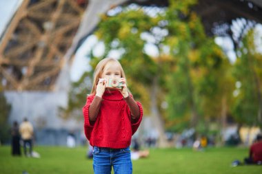 Paris, Fransa 'daki Eyfel Kulesi' nin yakınında tahta oyuncak kamerayla fotoğraf çeken sevimli anaokulu kızı. Mutlu çocuk sonbahar günü parkta oyuncaklarla oynuyor. Çocuk dışarıda sağlıklı atıştırmalıkları seviyor.