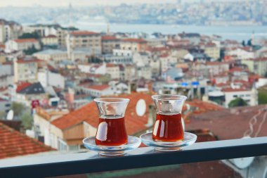 İstanbul, Türkiye 'nin Asya yakasındaki Uskudar ilçesinin çatıları manzaralı sıcak siyah çay dolu bir lale şeklinde iki Türk bardağı