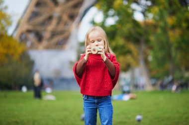 Paris, Fransa 'daki Eyfel Kulesi' nin yakınında tahta oyuncak kamerayla fotoğraf çeken sevimli anaokulu kızı. Mutlu çocuk sonbahar günü parkta oyuncaklarla oynuyor. Çocuk dışarıda sağlıklı atıştırmalıkları seviyor.