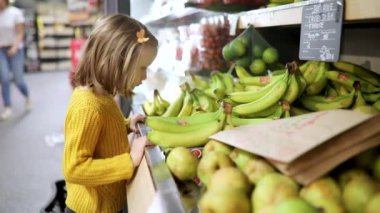 Süpermarkette muz seçen sevimli anaokulu kızı. Çocuk alışverişe gidiyor. Geniş yiyecek ya da marketteki çocuk.