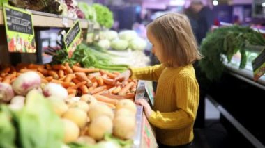 Süpermarkette havuç seçen sevimli anaokulu kızı. Çocuk alışverişe gidiyor. Geniş yiyecek ya da marketteki çocuk.