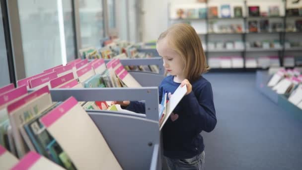 一个可敬的学龄前女孩坐在市立图书馆的地板上看书 — 图库视频影像