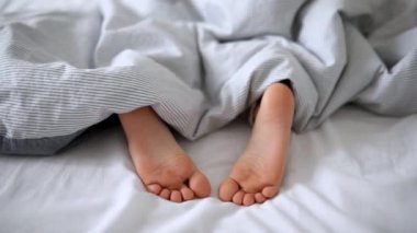 Battaniyeyle kaplı küçük çocuk ayakları. Çocuk rahat bir yatakta uyuyor. Sabah erkenden evde.