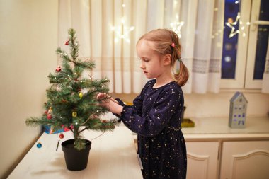 Küçük Noel ağacını evde minyatür oyuncaklarla süsleyen sevimli anaokulu kızı.