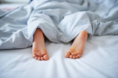 Battaniyeyle kaplı küçük çocuk ayakları. Çocuk rahat bir yatakta uyuyor. Sabah erkenden evde.