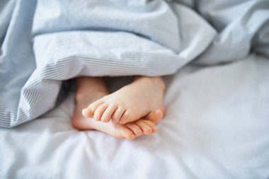 Battaniyeyle kaplı küçük çocuk ayakları. Çocuk rahat bir yatakta uyuyor. Sabah erkenden evde.