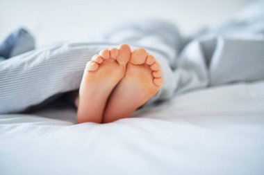 Battaniyeyle kaplı küçük çocuk ayakları. Çocuk rahat bir yatakta uyuyor. Sabah erkenden evde.