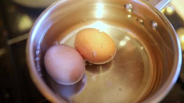 Gaz ocağındaki bir tencerede sıcak suda iki yumurta kaynıyor. Evde yemek yapmak. Protein yemeği.