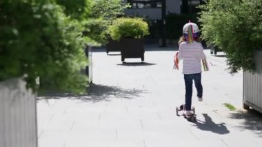 Güneşli bir bahar gününde şehir parkında scooterıyla gezen sevimli anaokulu kızı. Tekboynuz kasklı şirin çocuk scooter kullanıyor. Çocuklar için aktif eğlence ve açık hava sporu