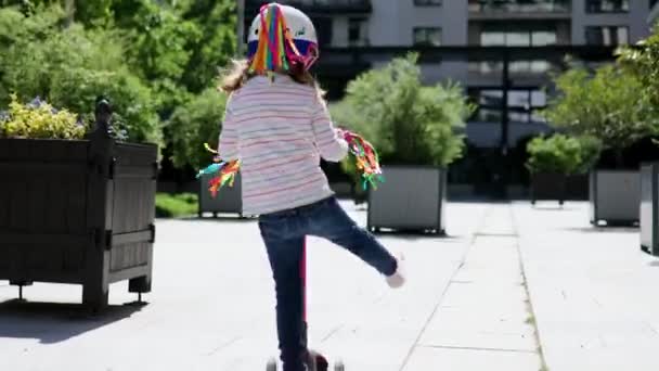 공원에서 스쿠터를 다니는 유니콘 헬멧을 귀여운 아이가 스쿠터를 있습니다 어린이들을 — 비디오