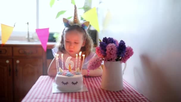6歳の誕生日を祝い ろうそくを吹き飛ばして願いを叶えるユニコーンの髪飾りを持つ幸せな少女 — ストック動画