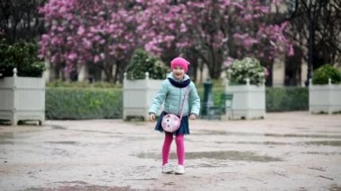 Fransa 'nın Paris kentinde yağmurlu bir günde pembe manolyaların tadını çıkaran sevimli anaokulu kızı.