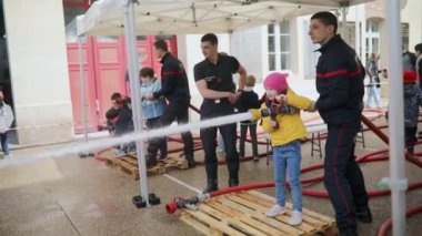 PARIS, FRANCE - 4 Mayıs 2024: Anaokulu öğrencisi kız, Fransa 'nın Paris şehrinde bir itfaiye istasyonunun açık günü yangın hortumu tutan ve su sıçratan bir itfaiyeci gibi davranıyor.