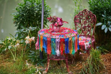 Renkli masa örtüsüyle kaplı güzel bir masa ve su kenarındaki bir kafede bir demet çiçek..