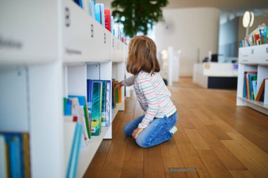 Belediye kütüphanesinde kitap seçen beş yaşında bir kız..