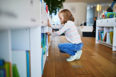 Belediye kütüphanesinde kitap seçen beş yaşında bir kız..