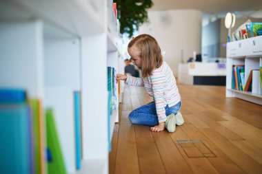 Belediye kütüphanesinde kitap seçen beş yaşında bir kız..