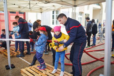 PARIS, FRANCE - 4 Mayıs 2024: Anaokulu öğrencisi kız, Fransa 'nın Paris şehrinde bir itfaiye istasyonunun açık günü yangın hortumu tutan ve su sıçratan bir itfaiyeci gibi davranıyor.