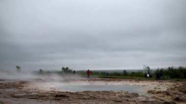 STROKUR, ICELAND - 13 Temmuz 2024: İzlanda 'da sisli bir yağmurlu günde Strokkur gayzer patlaması bekleyen insanlar