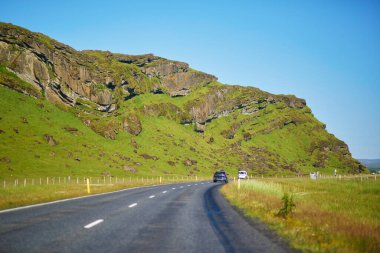 İzlanda 'nın güzel manzarasıyla çevrili bir yolda giden araba.