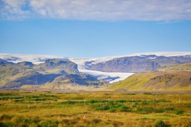 Yeşil tarlaları olan güzel doğa manzarası ve Güney İzlanda 'da buzlu ve karlı görkemli uçurumlar.