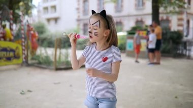 Kedi suratlı küçük anaokulu kızı dışarıda köpük üflüyor. Çocuklar boyayla yüzleşir. Çocuklar için yaratıcı etkinlikler