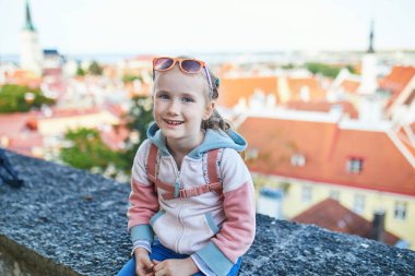 Sırt çantalı sevimli anaokulu kızı Estonya 'nın Tallinn şehrinin eski manzarasının tadını çıkarıyor.