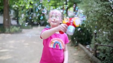 Parkta sabun köpüğü üfleyen sevimli mutlu küçük kız..