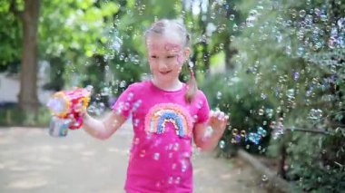 Parkta sabun köpüğü üfleyen sevimli mutlu küçük kız..