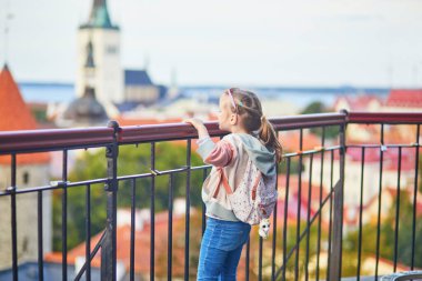 Sırt çantalı sevimli anaokulu kızı Estonya 'nın Tallinn şehrinin eski manzarasının tadını çıkarıyor.