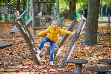 Neşeli küçük kız Paris, Fransa 'daki sonbahar parkında oyun alanında eğleniyor.