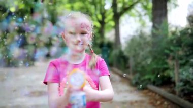 Parkta sabun köpüğü üfleyen sevimli mutlu küçük kız..