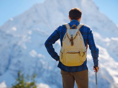 Irkis Vadisi 'nden, Arkhyz' den, Karachay-Cherkessia 'dan, Kuzey Kafkasya' dan. Mavi gökyüzü, bulutlar ve Kafkasya nehri yakınlarındaki güzel ormanla karlı dağ vadisinde yürüyüş yapan bir adam..