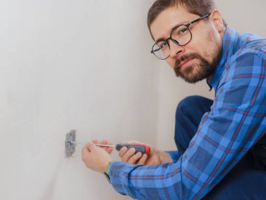 Mavi takım elbiseli genç adam apartman dairesinde çalışıyor. Ev yenileme konsepti. Elektrik soketi kuran elektrikçi