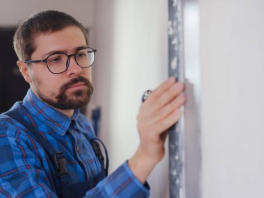 Genç yetişkin erkek eli spatula kullanıyor ve beyaz duvarı taze macunla kaplıyor. - Yakın çekim. Ev onarımı..