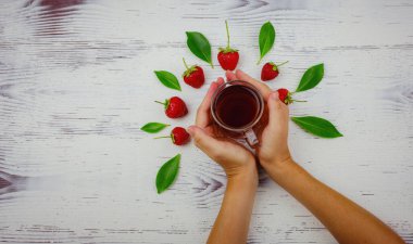 Taze organik çilekler ve cam bardakta siyah çay. Kadın eli, beyaz arka planda. Vejetaryen sağlıklı gıda konsepti.