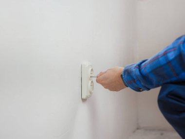 Mavi takım elbiseli genç adam apartman dairesinde çalışıyor. Ev yenileme konsepti. Elektrik soketi kuran elektrikçi