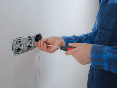 Mavi takım elbiseli genç adam apartman dairesinde çalışıyor. Ev yenileme konsepti. Elektrik soketi kuran elektrikçi