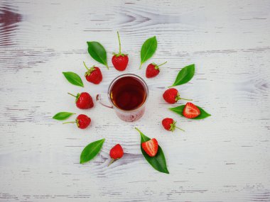 Taze organik çilekler ve cam bardakta siyah çay. Kadın eli, beyaz arka planda. Vejetaryen sağlıklı gıda konsepti.