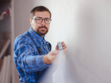 Mavi takım elbiseli genç adam beyaz arka planda izole edilmiş şerit tutuyor. Aletler, aksesuarlar, yenileme dairesi araçları, seçici odaklanma